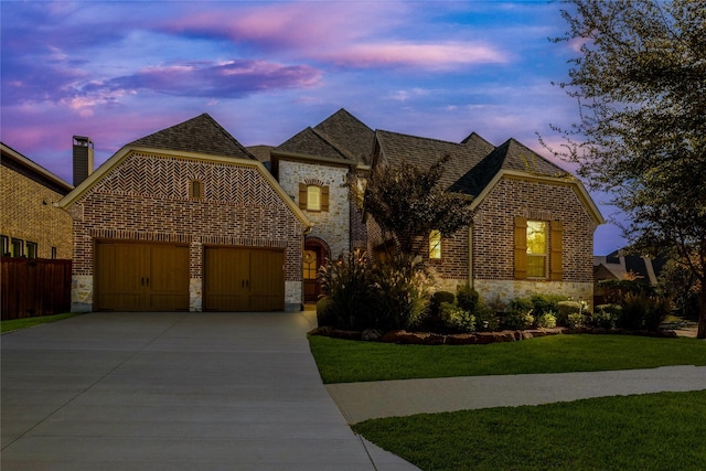 view of front of home with a garage, concrete driveway, stone siding, a front lawn, and brick siding