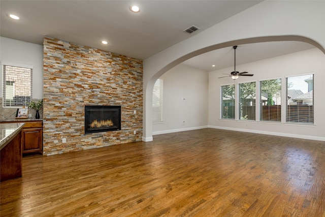 living area featuring arched walkways, visible vents, a ceiling fan, a stone fireplace, and wood finished floors