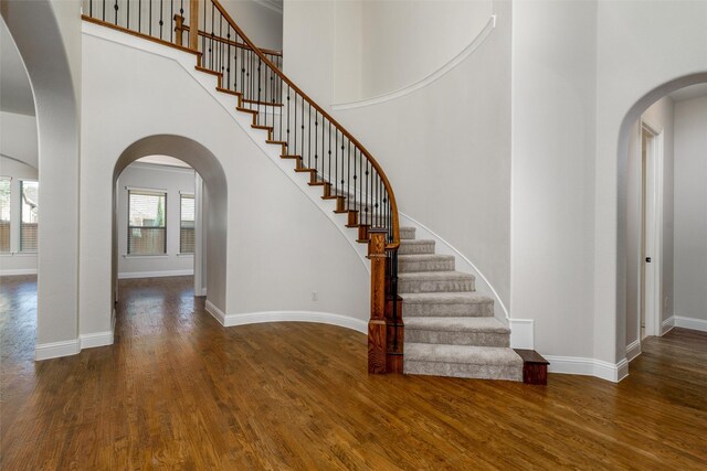 stairway featuring a towering ceiling, baseboards, and wood finished floors