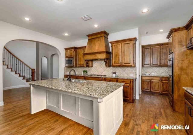 kitchen featuring stainless steel appliances, premium range hood, a sink, and brown cabinets