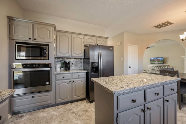 kitchen with gray cabinets, decorative backsplash, a kitchen island, and appliances with stainless steel finishes