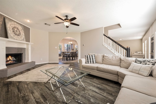 living room with a fireplace, a textured ceiling, dark hardwood / wood-style flooring, and ceiling fan