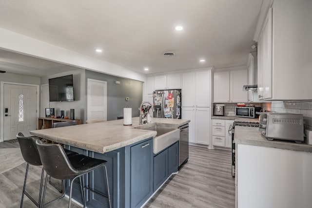 kitchen with a kitchen island with sink, white cabinets, sink, appliances with stainless steel finishes, and light hardwood / wood-style floors