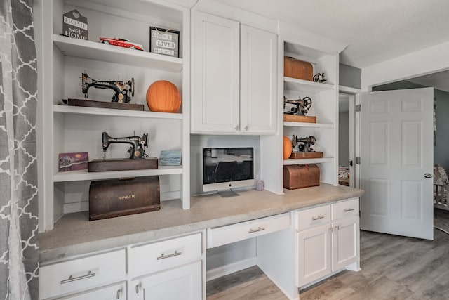 kitchen featuring white cabinets, light wood-type flooring, and built in desk