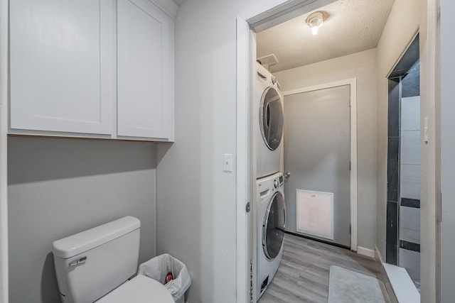 clothes washing area with a textured ceiling, light hardwood / wood-style flooring, and stacked washer / drying machine