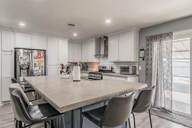 kitchen featuring white cabinets, wall chimney range hood, stainless steel appliances, and a wealth of natural light