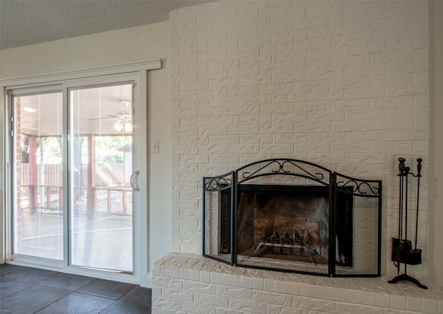 interior details with tile patterned floors, ceiling fan, a textured ceiling, and a brick fireplace