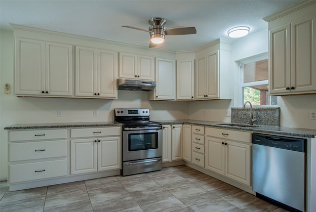 kitchen with appliances with stainless steel finishes, ceiling fan, dark stone counters, and sink