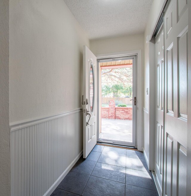 doorway to outside featuring dark tile patterned flooring and a textured ceiling