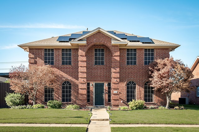 colonial home featuring cooling unit, a front yard, and solar panels