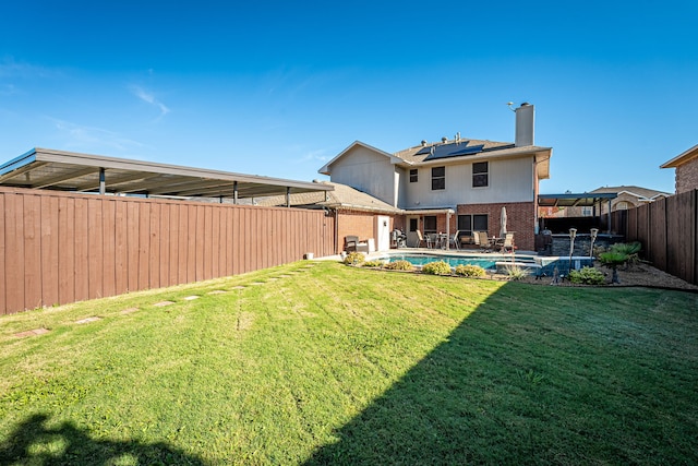 rear view of house with solar panels, a yard, and a fenced in pool