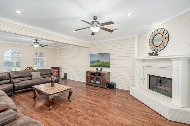 living room featuring hardwood / wood-style floors, ceiling fan, crown molding, and a brick fireplace