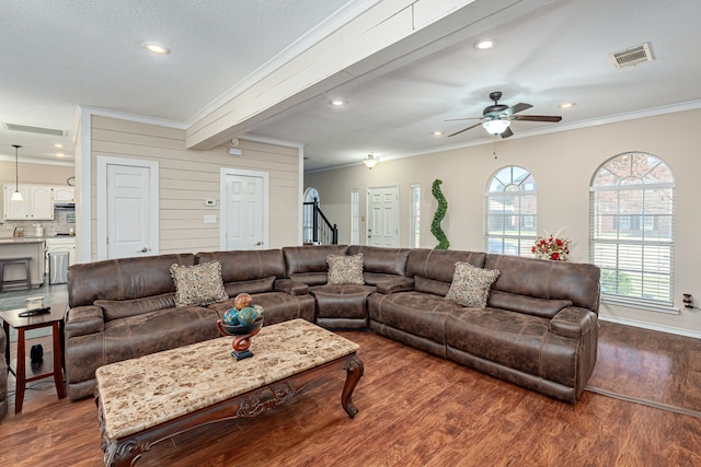 living room with ceiling fan, dark wood-type flooring, beamed ceiling, wooden walls, and ornamental molding