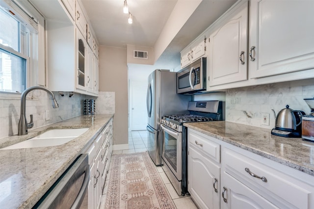 kitchen featuring appliances with stainless steel finishes, backsplash, sink, light tile patterned floors, and white cabinetry