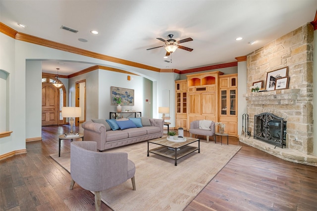 living room featuring wood-type flooring, a stone fireplace, ceiling fan, and ornamental molding