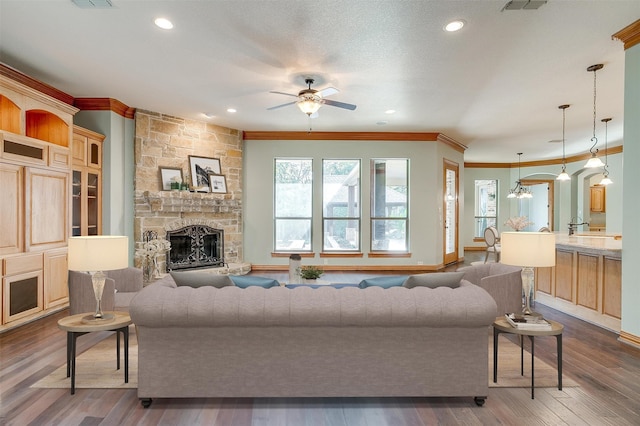 living room with ceiling fan, a stone fireplace, dark hardwood / wood-style floors, a textured ceiling, and ornamental molding