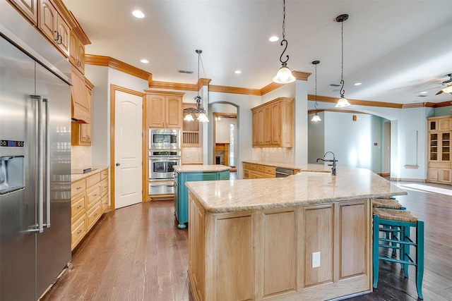 kitchen with tasteful backsplash, kitchen peninsula, built in appliances, decorative light fixtures, and light brown cabinetry