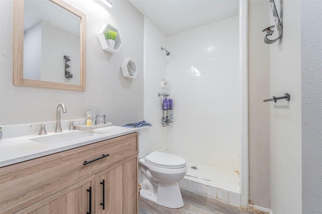 bathroom featuring hardwood / wood-style floors, vanity, a tile shower, and toilet