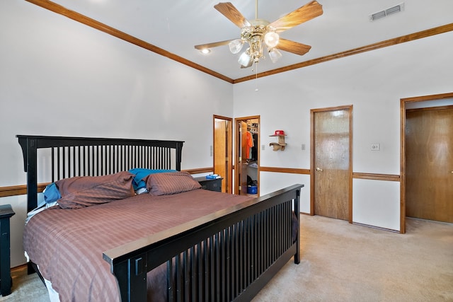 carpeted bedroom with a spacious closet, ceiling fan, and ornamental molding