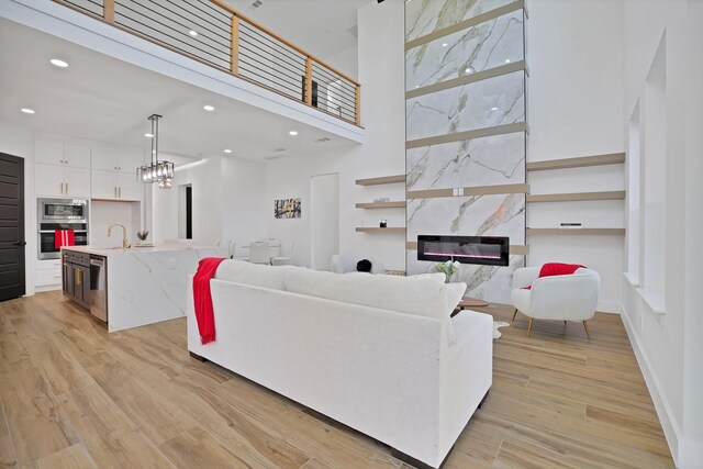 living room featuring sink, a high ceiling, an inviting chandelier, light hardwood / wood-style floors, and a fireplace