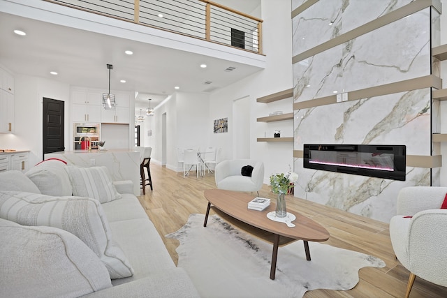 living room featuring a high end fireplace, a high ceiling, light wood-type flooring, and a notable chandelier