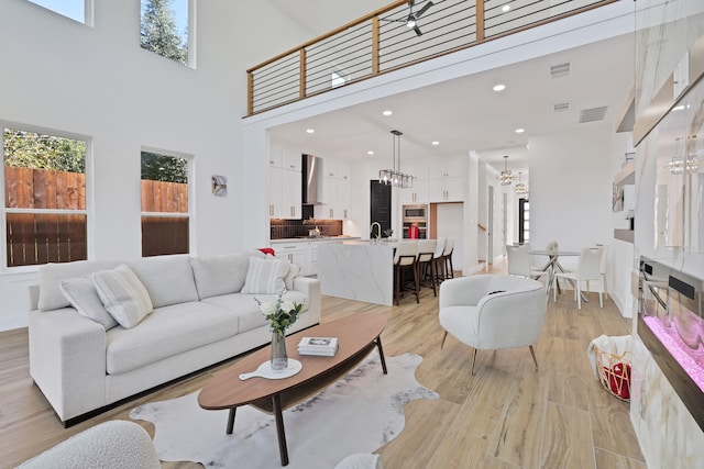 living room featuring light wood-type flooring, a towering ceiling, sink, and an inviting chandelier