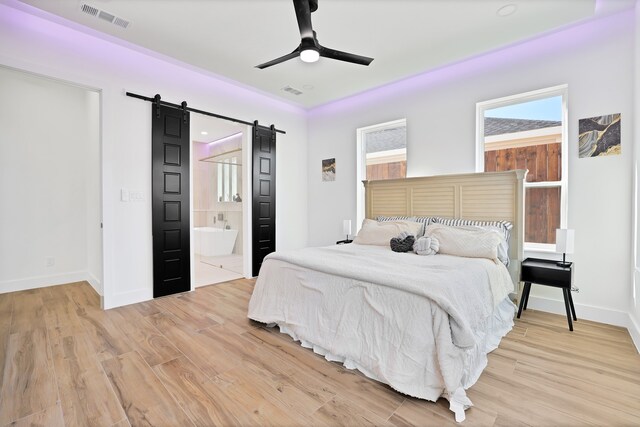 bedroom with a barn door, ensuite bath, light hardwood / wood-style flooring, and ceiling fan