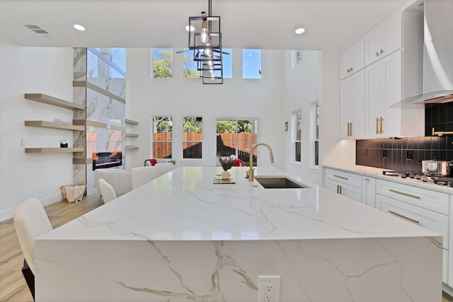 kitchen with light stone countertops, stainless steel gas cooktop, wall chimney range hood, sink, and light hardwood / wood-style flooring