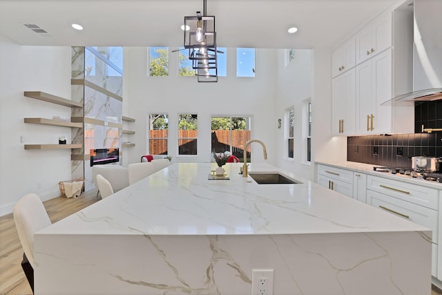 kitchen with wall chimney exhaust hood, stainless steel gas stovetop, sink, and light stone countertops