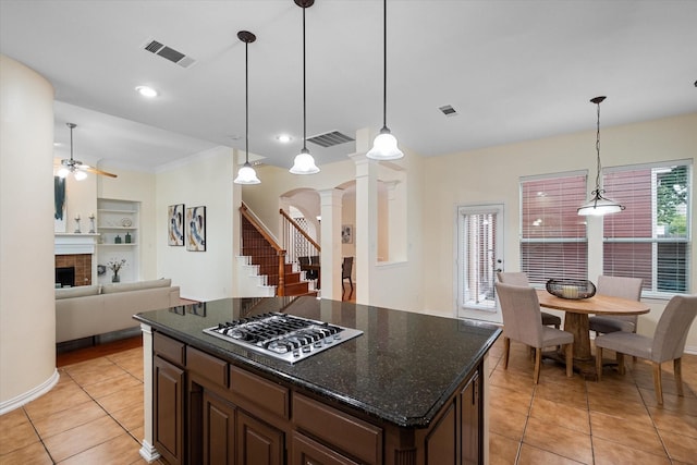 kitchen featuring stainless steel gas stovetop, hanging light fixtures, dark brown cabinets, a kitchen island, and decorative columns