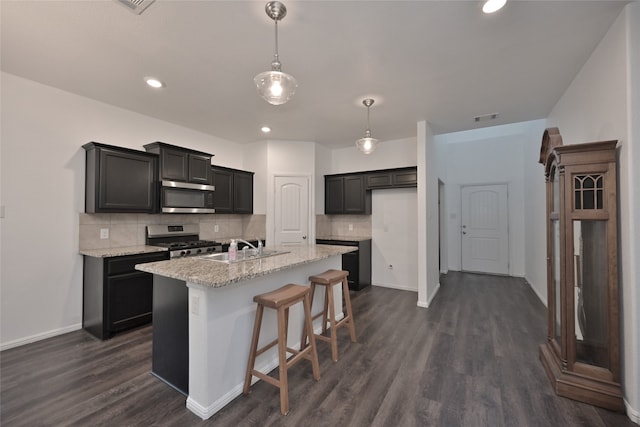 kitchen featuring light stone countertops, stainless steel appliances, tasteful backsplash, dark hardwood / wood-style floors, and a center island with sink