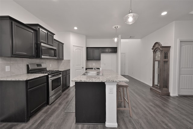 kitchen with appliances with stainless steel finishes, sink, dark hardwood / wood-style floors, hanging light fixtures, and an island with sink