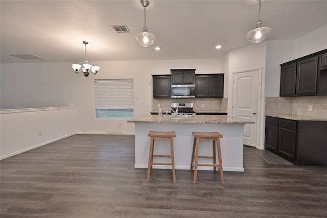 kitchen featuring decorative backsplash, stainless steel appliances, a kitchen island with sink, and dark wood-type flooring