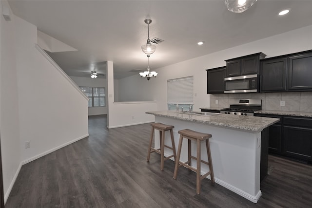 kitchen with backsplash, a breakfast bar, stainless steel appliances, dark wood-type flooring, and a center island with sink