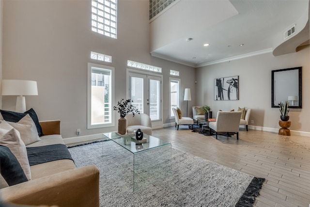 living room with french doors, a towering ceiling, light hardwood / wood-style floors, and ornamental molding