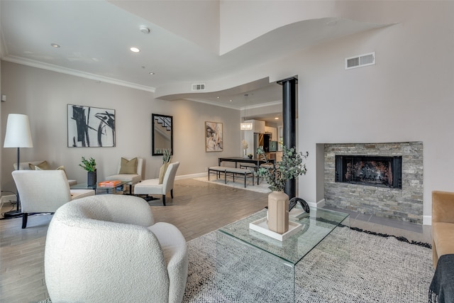 living room featuring a stone fireplace, crown molding, and light hardwood / wood-style flooring