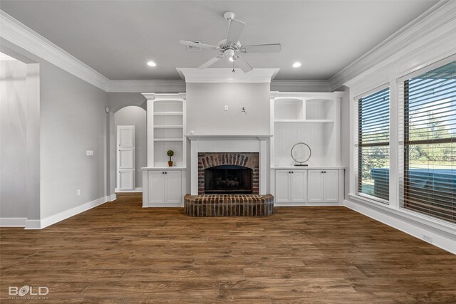 unfurnished living room featuring ceiling fan, ornamental molding, dark wood-type flooring, and a brick fireplace