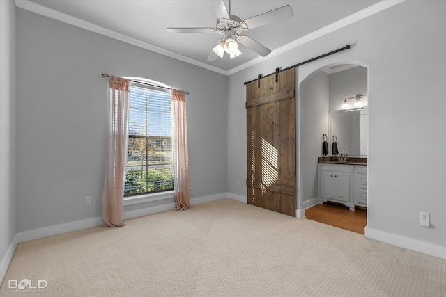 unfurnished bedroom featuring carpet, ceiling fan, a barn door, ornamental molding, and connected bathroom