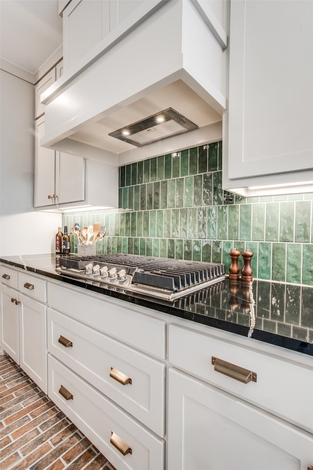 kitchen with decorative backsplash, custom range hood, cooktop, and white cabinetry