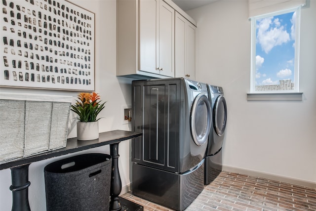 clothes washing area featuring cabinets, a healthy amount of sunlight, and washing machine and dryer