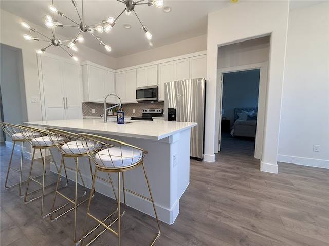 kitchen with appliances with stainless steel finishes, a kitchen breakfast bar, white cabinets, decorative backsplash, and a large island with sink