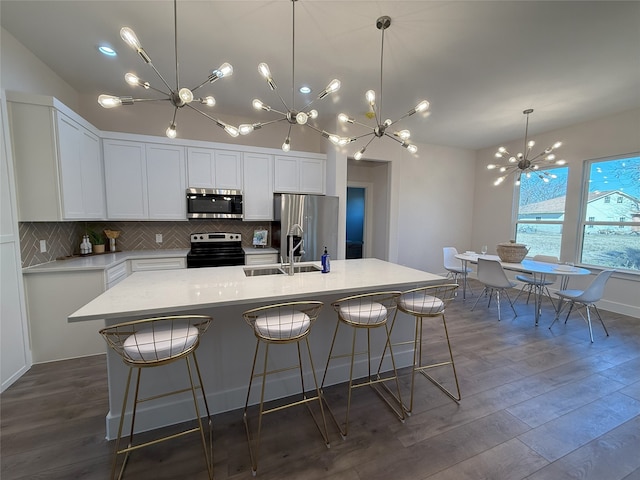 kitchen with dark hardwood / wood-style floors, white cabinetry, sink, stainless steel appliances, and a center island with sink