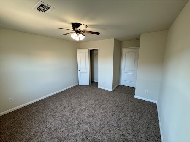 unfurnished bedroom featuring dark colored carpet, ceiling fan, a walk in closet, and a closet