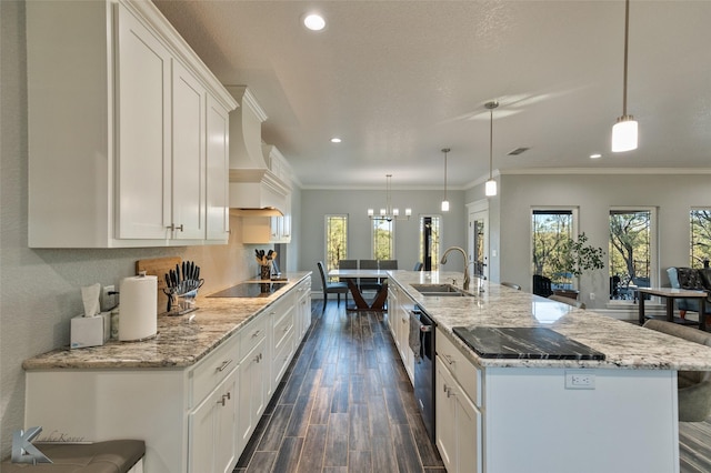 kitchen with a large island with sink, sink, pendant lighting, and white cabinets