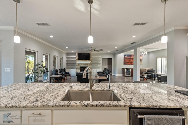 kitchen with sink, built in features, hanging light fixtures, light stone counters, and a fireplace