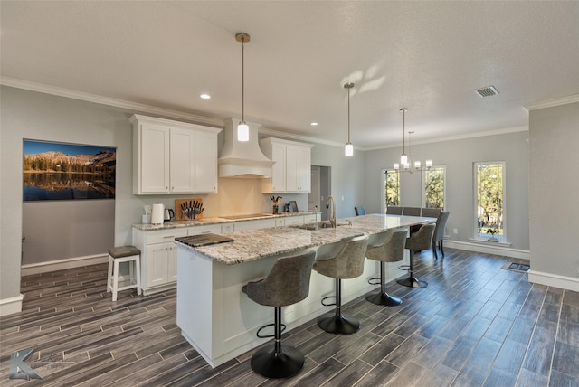 kitchen with custom exhaust hood, a breakfast bar area, an island with sink, and white cabinets