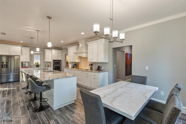 kitchen featuring a large island, decorative light fixtures, custom range hood, and black appliances