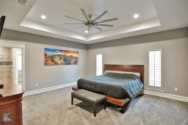 carpeted bedroom featuring a raised ceiling, ceiling fan, and ensuite bathroom