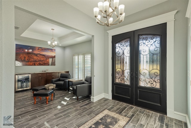 foyer with a raised ceiling, beverage cooler, an inviting chandelier, and french doors