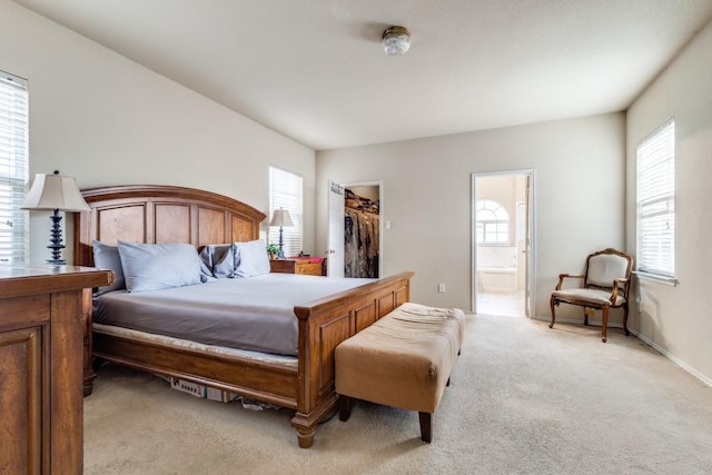 bedroom with a walk in closet, multiple windows, light colored carpet, and connected bathroom